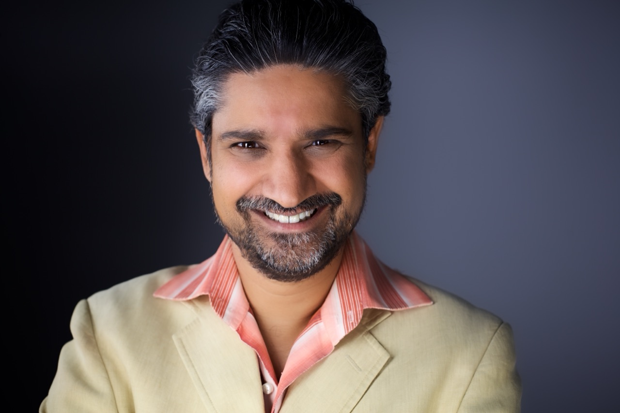 Kuldip Korotana smiling in a beige jacket and coral shirt
